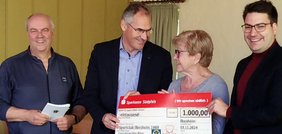 Landrat Dietmar Seefeldt (Zweiter von links) und Benjamin Hirsch, Vorstandsmitglied der Sparkasse Südpfalz (rechts), übergeben dem Vereinsvorsitzenden des SC Ilbesheim Manfred Mühlan und Schatzmeisterin Ingrid Kostrzewa den Spendenscheck.