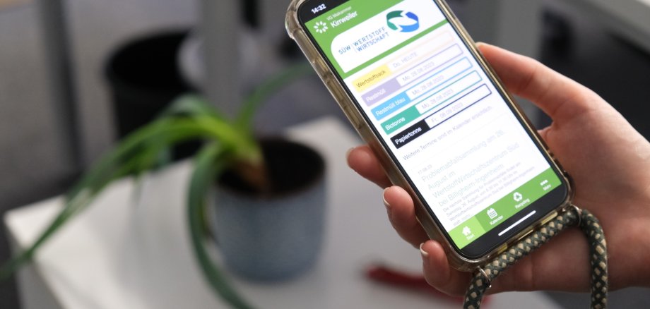 Eine Hand hält ein Smartphone, darauf die geöffnete Wertstoff-App.