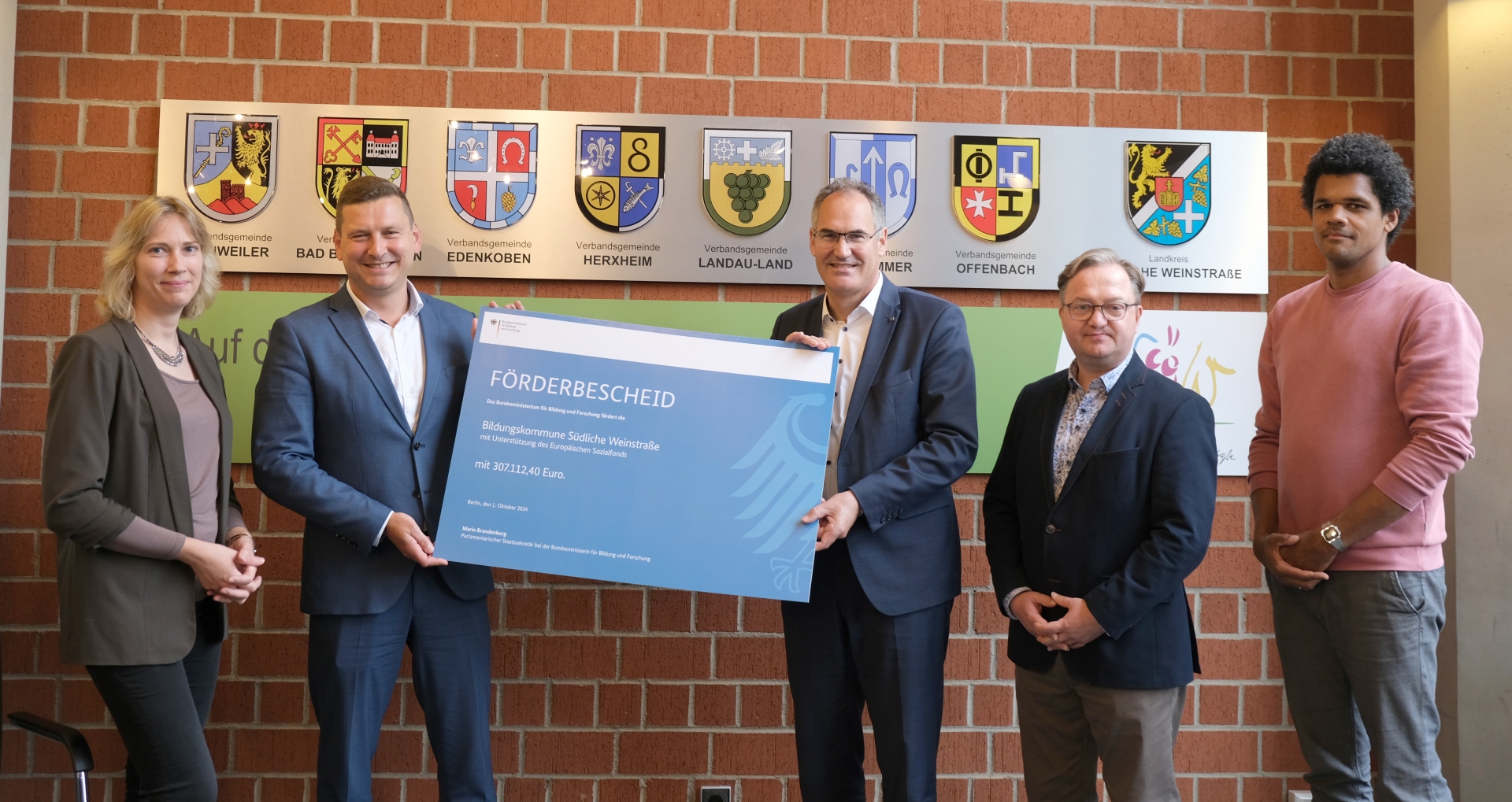 Bei der Bescheidübergabe von links nach rechts: kvhs-Leiterin Monika Kukyte, Parlamentarischer Staatssekretär Mario Brandenburg, Landrat Dietmar Seefeldt, stellvertretender Abteilungsleiter „Schulen“ Ronny Bodenseh und stellvertretender KMS-Leiter Thomas Weiland. Foto: KV SÜW Bei der Bescheidübergabe von links nach rechts: kvhs-Leiterin Monika Kukyte, Parlamentarischer Staatssekretär Mario Brandenburg, Landrat Dietmar Seefeldt, stellvertretender Abteilungsleiter „Schulen“ Ronny Bodenseh und stellvertretender KMS-Leiter Thomas Weiland. Brandenburg und Seefeldt halten gemeinsam den großen symbolischen Bescheid.