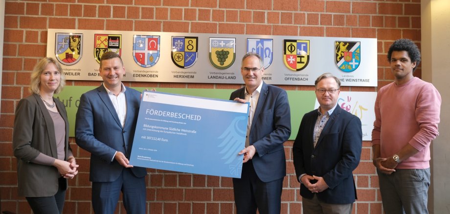 Bei der Bescheidübergabe von links nach rechts: kvhs-Leiterin Monika Kukyte, Parlamentarischer Staatssekretär Mario Brandenburg, Landrat Dietmar Seefeldt, stellvertretender Abteilungsleiter „Schulen“ Ronny Bodenseh und stellvertretender KMS-Leiter Thomas Weiland. Brandenburg und Seefeldt halten gemeinsam den großen symbolischen Bescheid.