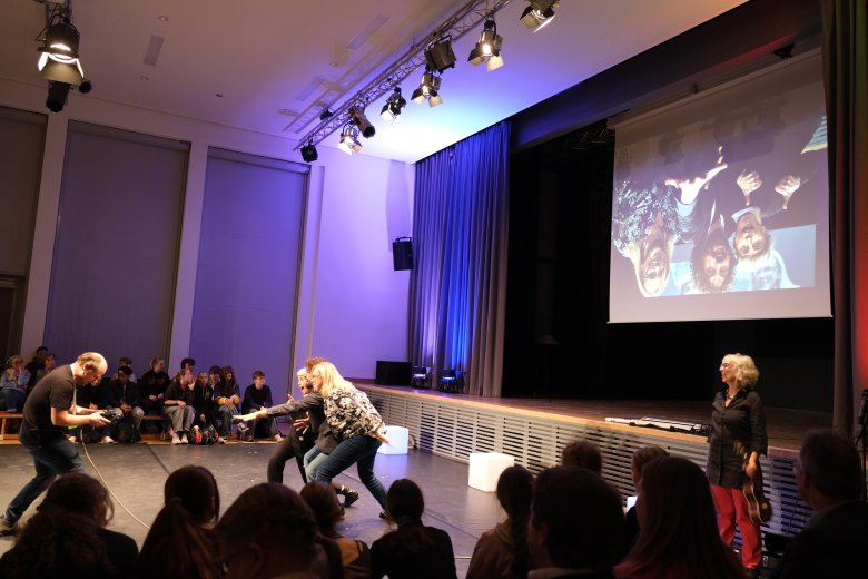 Kopfüber stand das Bild beim Eröffnungsbeitrag und „kopfüber“ lautet das Motto des dreitätigen Festivals. Foto: KV SÜW Schauspieler blicken in eine Kamera, dahinter ihr Bild kopfüber.