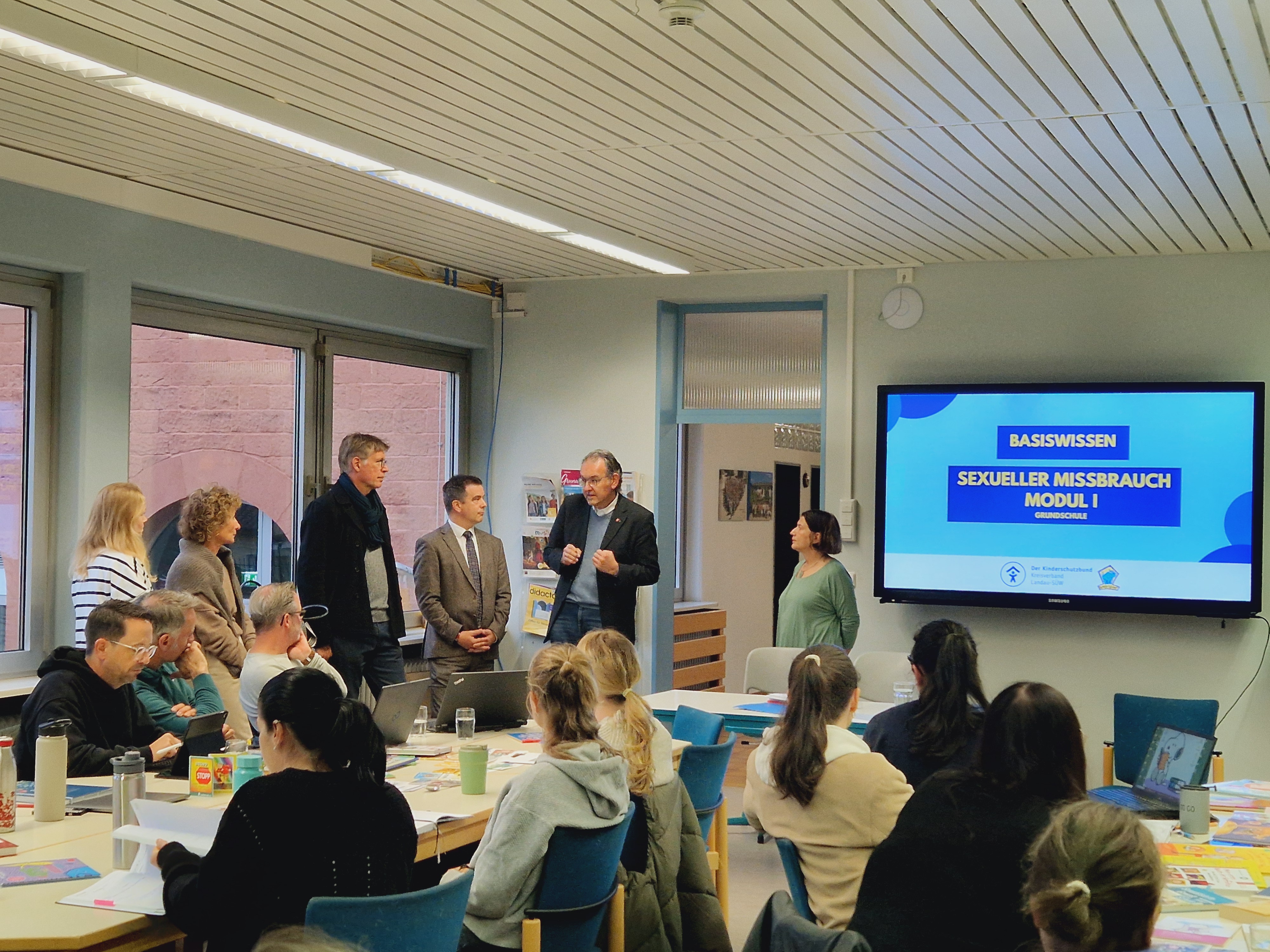 Menschen in einem Klassenraum vor einer digitalen Tafel.