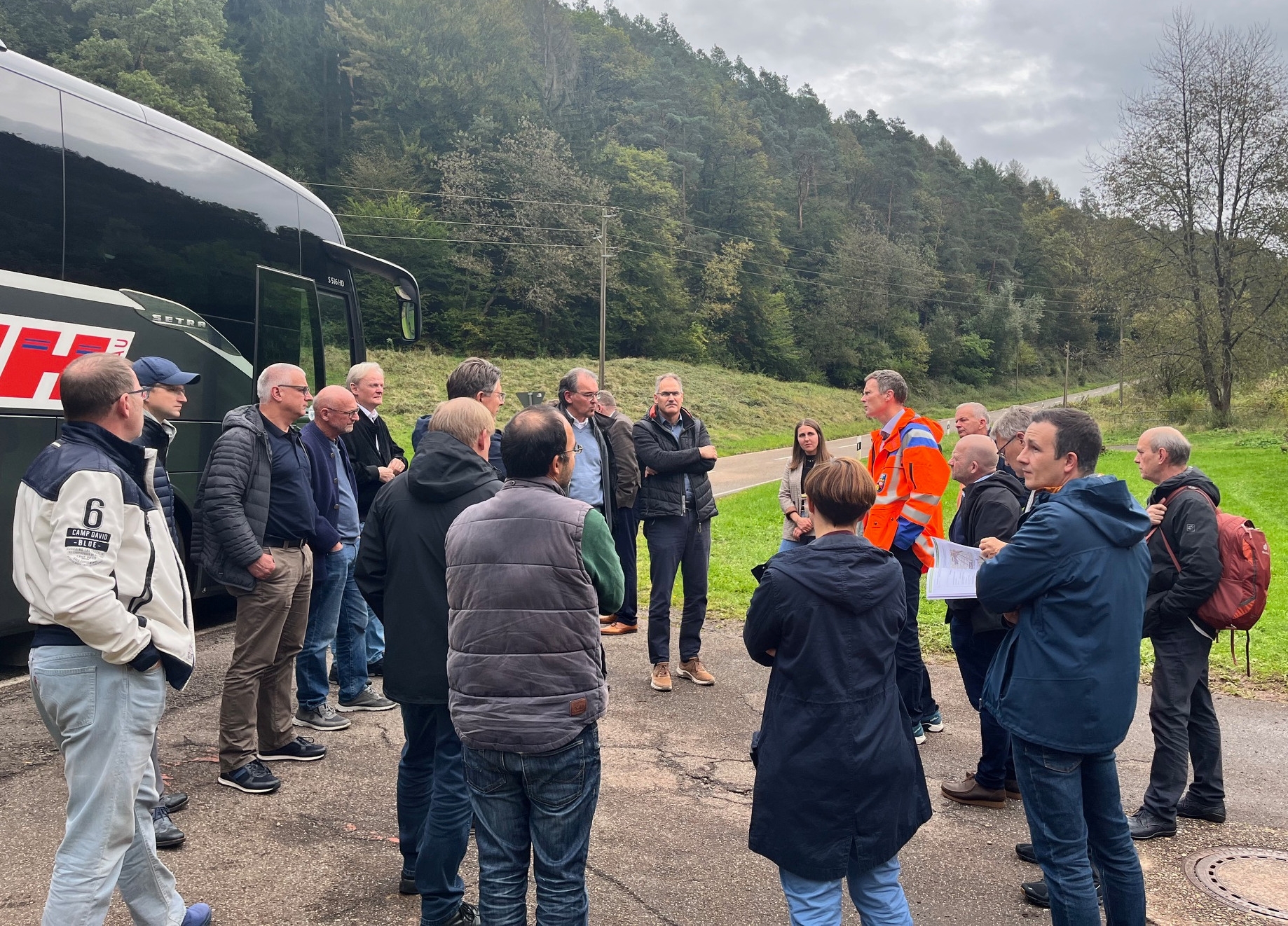 Mitglieder des Kreisausschusses stehen in einer Gruppe zusammen und hören den Ausführungen eines Vertreters des Landesbetriebs Mobilität zu. Der Austausch findet an einer Straße im Grünen statt, im Rahmen einer Rundfahrt durch den Landkreis Südliche Weinstraße, um den Zustand der Kreisstraßen zu begutachten.