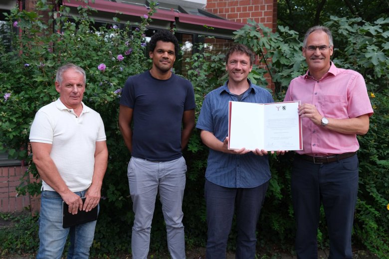 Landrat Dietmar Seefeldt, KMS-Schulleiter Adrian Rinck, stellvertretender KMS-Schulleiter Thomas Roscoe Weiland und Kreisbeigeordneter Werner Schreiner mit der Preisurkunde am Kreishaus SÜW (von rechts nach links). Foto: KV SÜW Landrat Dietmar Seefeldt, KMS-Schulleiter Adrian Rinck, stellvertretender KMS-Schulleiter Thomas Roscoe Weiland und Kreisbeigeordneter Werner Schreiner präsentieren die Preisurkunde am Kreishaus der Südlichen Weinstraße.