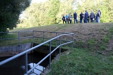 Eine Gruppe von Menschen besichtigt einen Teil des Hochwasserdamms bei Siebeldingen, mit einem nahegelegenen Wasserbauwerk im Vordergrund.