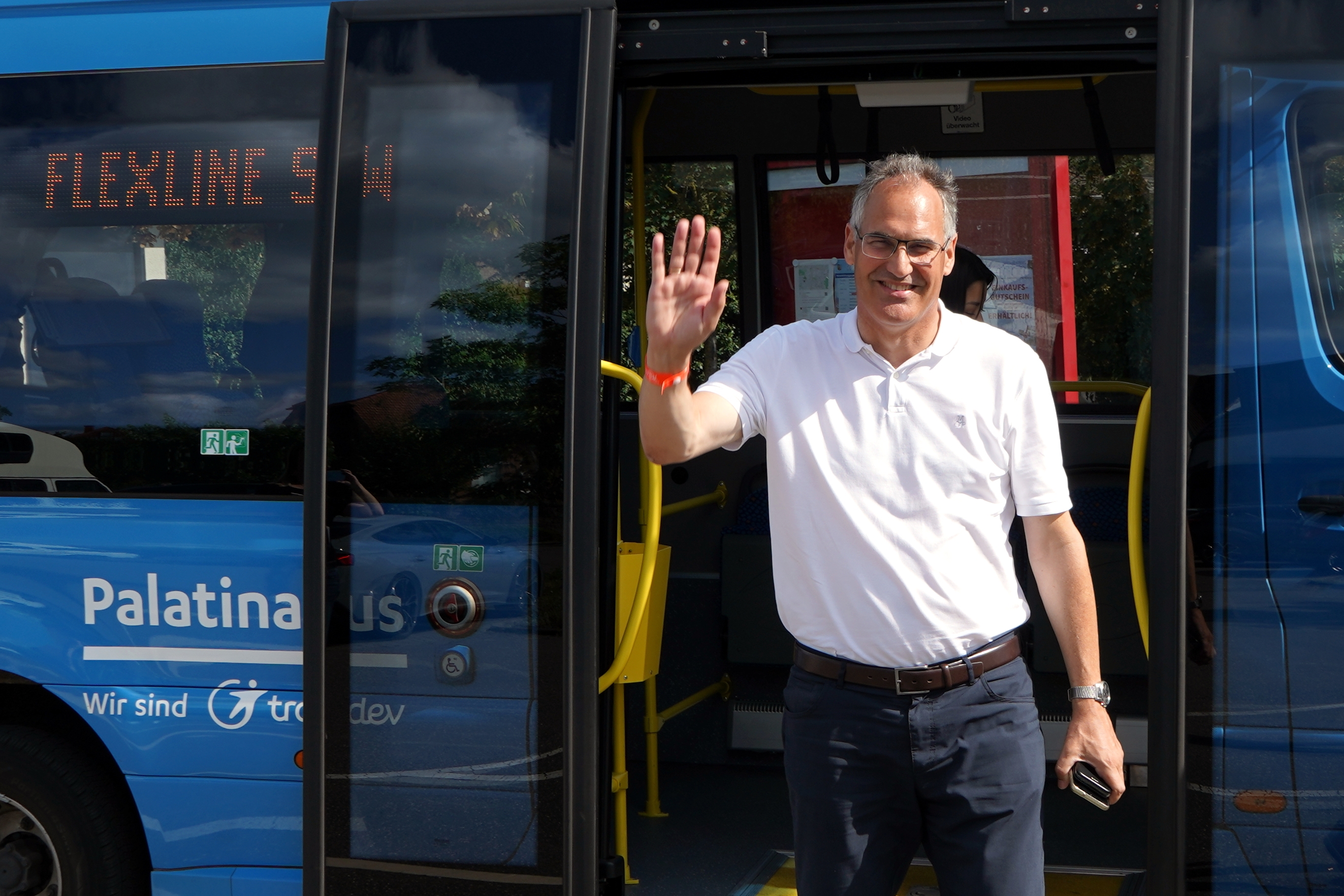 Ein Mann mit Handy in der Hand winkt, kommt gerade aus einem Kleinbus.