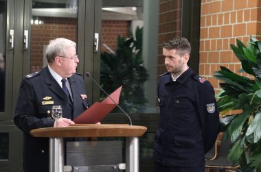 Hans-Georg Balthasar (links) zeichnete die scheidenden Kreisjugendfeuerwehrwarte aus, hier mit Daniel Hey. Foto: KV SÜW Hans-Georg Balthasar steht an einem Rednerpult und hält eine rote Dokumentenmappe in der Hand. Sein Blick richtet sich zu einem Feuerwehrangehörigen in Uniform, Daniel Hey, der neben dem Pult steht und ausgezeichnet wird.