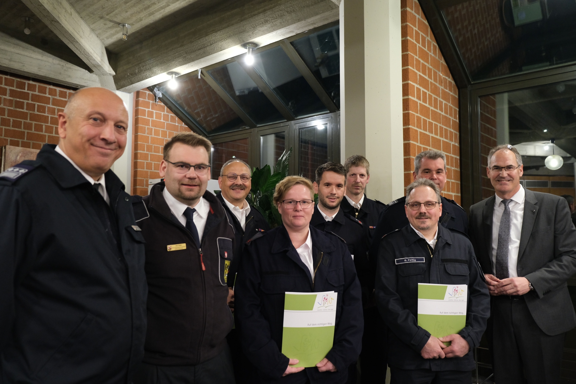 Gruppenfoto mehrerer Feuerwehrangehöriger in Uniform zusammen mit Landrat Dietmar Seefeldt. Einige halten grüne Mappen mit dem Logo des Landkreises Südliche Weinstraße in der Hand.