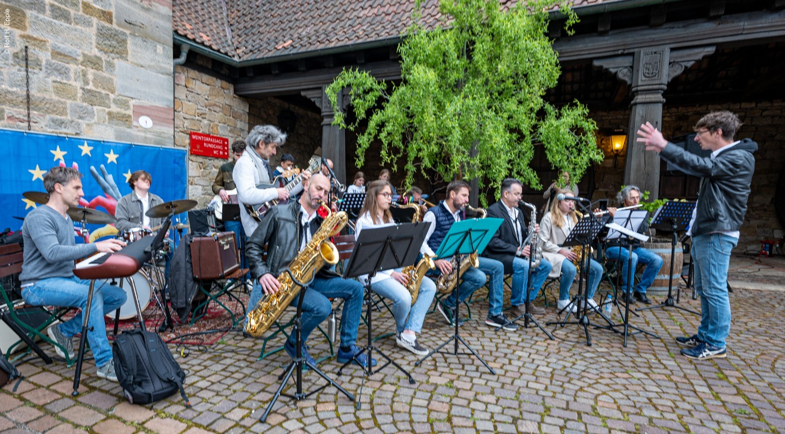 Ein großes Jazzensemble mit Saxophonen, Gitarre, Keyboard und Schlagzeug spielt unter der Leitung eines Dirigenten am Deutschen Weintor.
