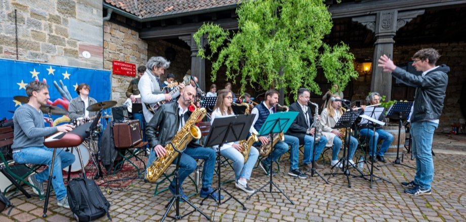 Ein großes Jazzensemble mit Saxophonen, Gitarre, Keyboard und Schlagzeug spielt unter der Leitung eines Dirigenten am Deutschen Weintor.