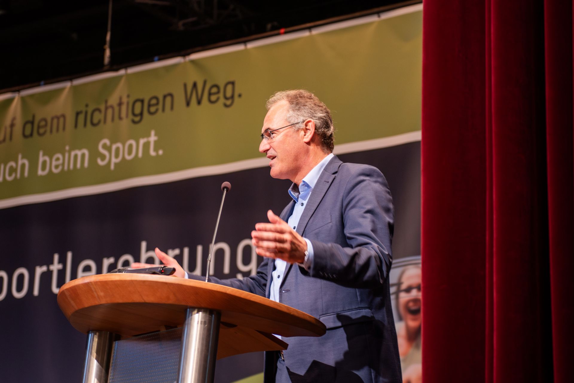 Landrat Dietmar Seefeldt spricht bei einer Sportlerehrung am Rednerpult. Im Hintergrund ist ein Banner mit dem Slogan der Kreisverwaltung Südliche Weinstraße zu sehen.