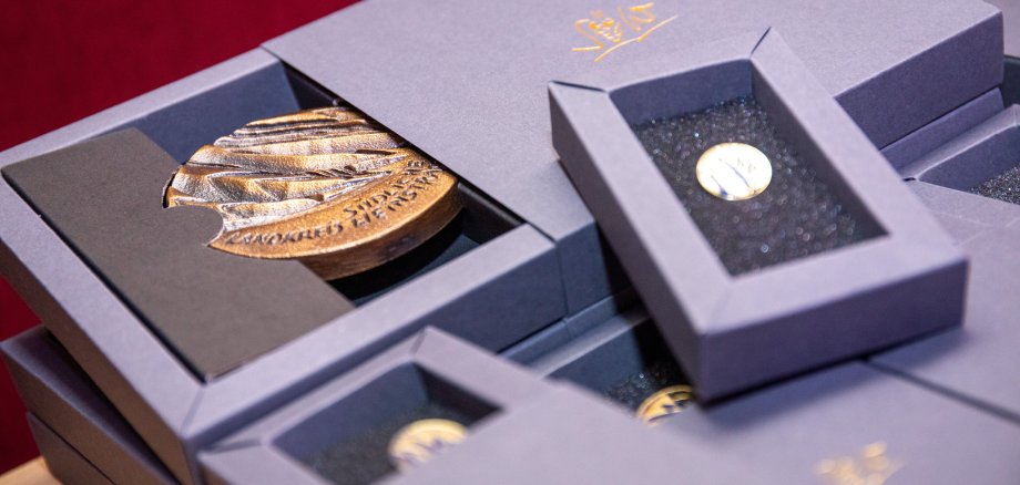 Einmal im Jahr ehrt der Landkreis SÜW die Ehrenamtlichen im Sport. Foto: Winstel Zu sehen sind eine Sportehrenplakette und eine Sportehrennadel in ihren Verpackungen liegend.