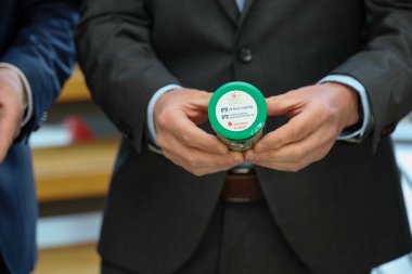 Ein Mann im dunklen Anzug hält eine grüne Notfalldose in beiden Händen. Auf dem Deckel der Dose sind die Logos und Namen der VR Bank Südpfalz, der VR Bank Südliche Weinstraße-Wasgau eG und der Sparkasse Südpfalz abgebildet.
