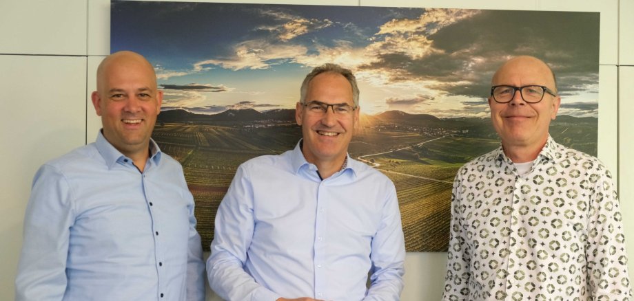 Martin Brandl, Landrat Kreis Germersheim, Dietmar Seefeldt, Landrat Kreis Südliche Weinstraße, und Dominik Geißler, Oberbürgermeister der Stadt Landau. Foto: KV SÜW Drei Personen vor einem Wandbild der Weinstraße.