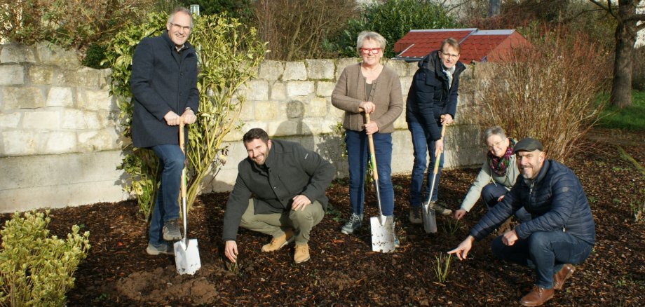 Halfen in Insheim mit beim Pflanzen der Rosen in Hainfeld (von links): Landrat Dietmar Seefeldt, Steven Barth, Leiter der Abteilung „Bauen und Umwelt“ der Kreisverwaltung, Hainfelds Ortsbürgermeisterin Ute Schweig, Daniel Salm, Bürgermeister der Verbandsgemeinde Edenkoben, Hedwig Klein und Matthias Bader, beide Ortsgemeinderatsmitglieder. Foto: KV SÜW Mehrere Personen, teilweise mit Spaten in der Hand, stehen neben frisch gepflanzten Rosen in einem Blumenbeet und lächeln in die Kamera.