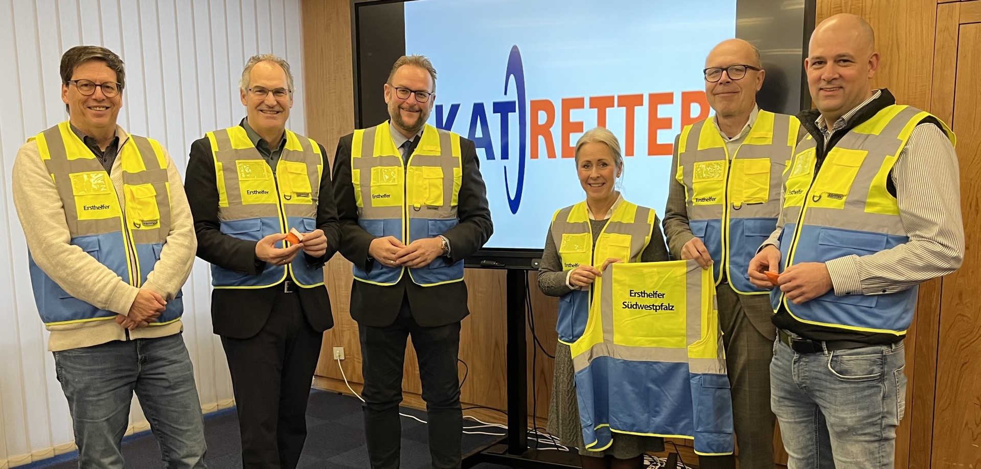 Sechs Personen stehen nebeneinander und lächeln in die Kamera. Sie alle tragen eine gelbe Weste, auf der "Ersthelfer" steht.