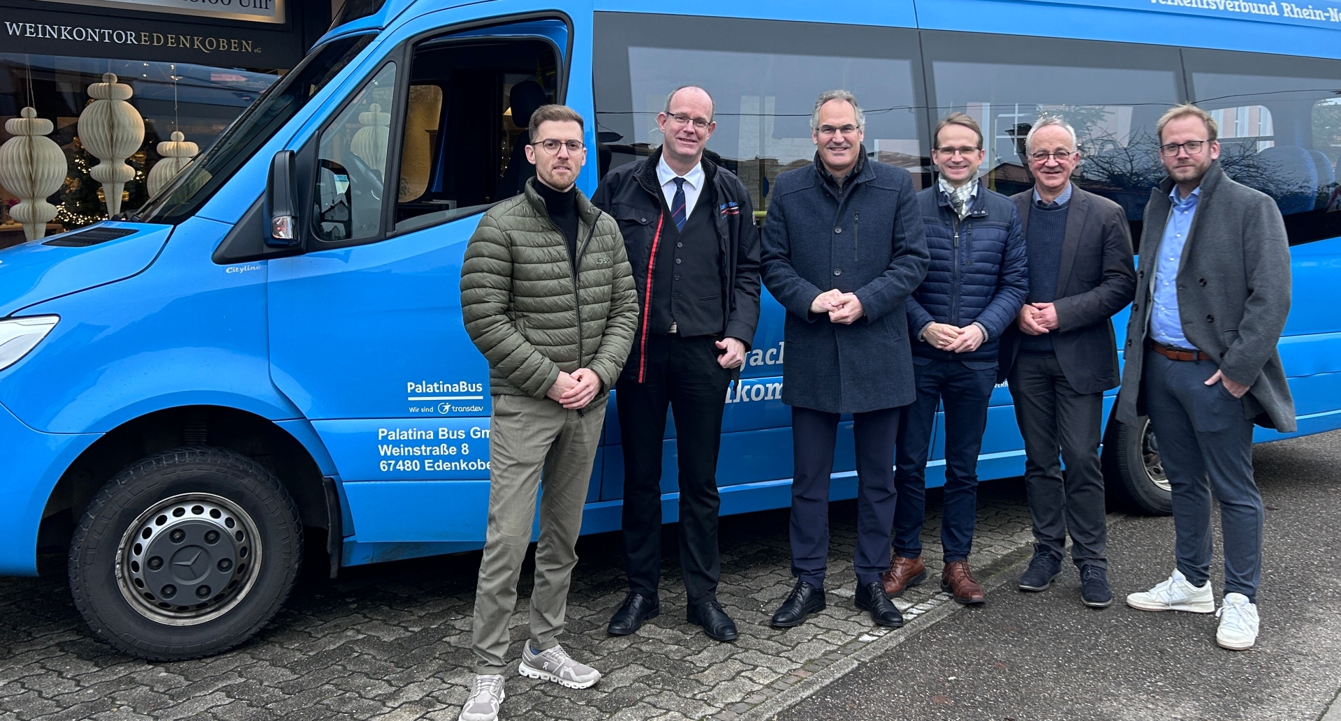 Sechs Männer stehen vor einem hellblauen Kleinbus.