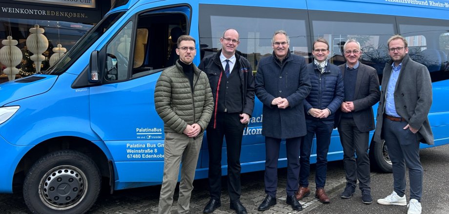 Von links: Benjamin Klar, ÖPNV-Referent des Landkreises SÜW, Marcus Weigl, Geschäftsführer von PALATINA-BUS, Landrat Dietmar Seefeldt, Daniel Salm, Bürgermeister der Verbandsgemeinde (VG) Edenkoben, Erster Beigeordneter der VG Eberhard Frankmann sowie Beigeordneter der VG Daniel Poth mit dem Kleinbus an der virtuelle Haltestelle Weinstraße 130 in Edenkoben. Foto: VG Edenkoben Sechs Männer stehen vor einem hellblauen Kleinbus.