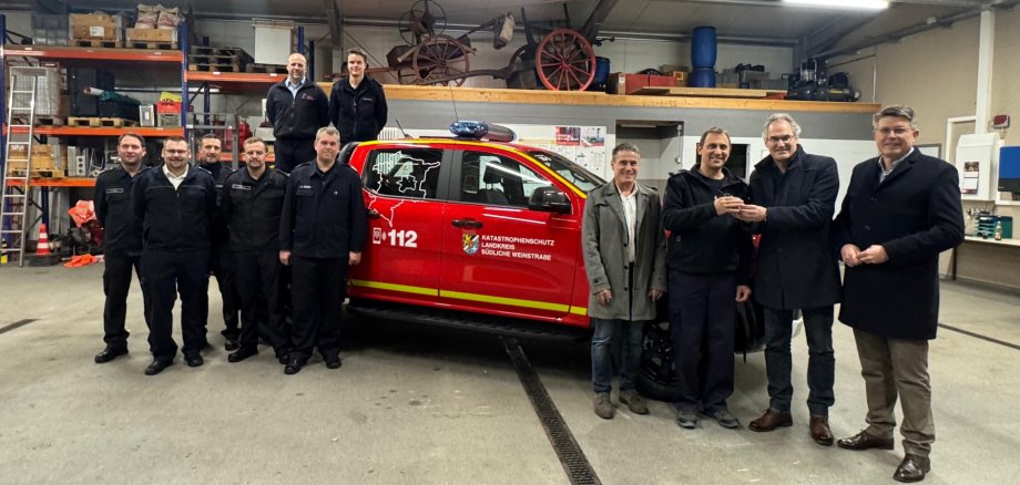 Mehrere Funktionsträger aus Kommunalpolitik und dem Brand- und Katastrophenschutz im Kreis SÜW stehen vor dem neuen KatSchutz-Fahrzeug beziehungsweise auf der Laderampe des Pickup.