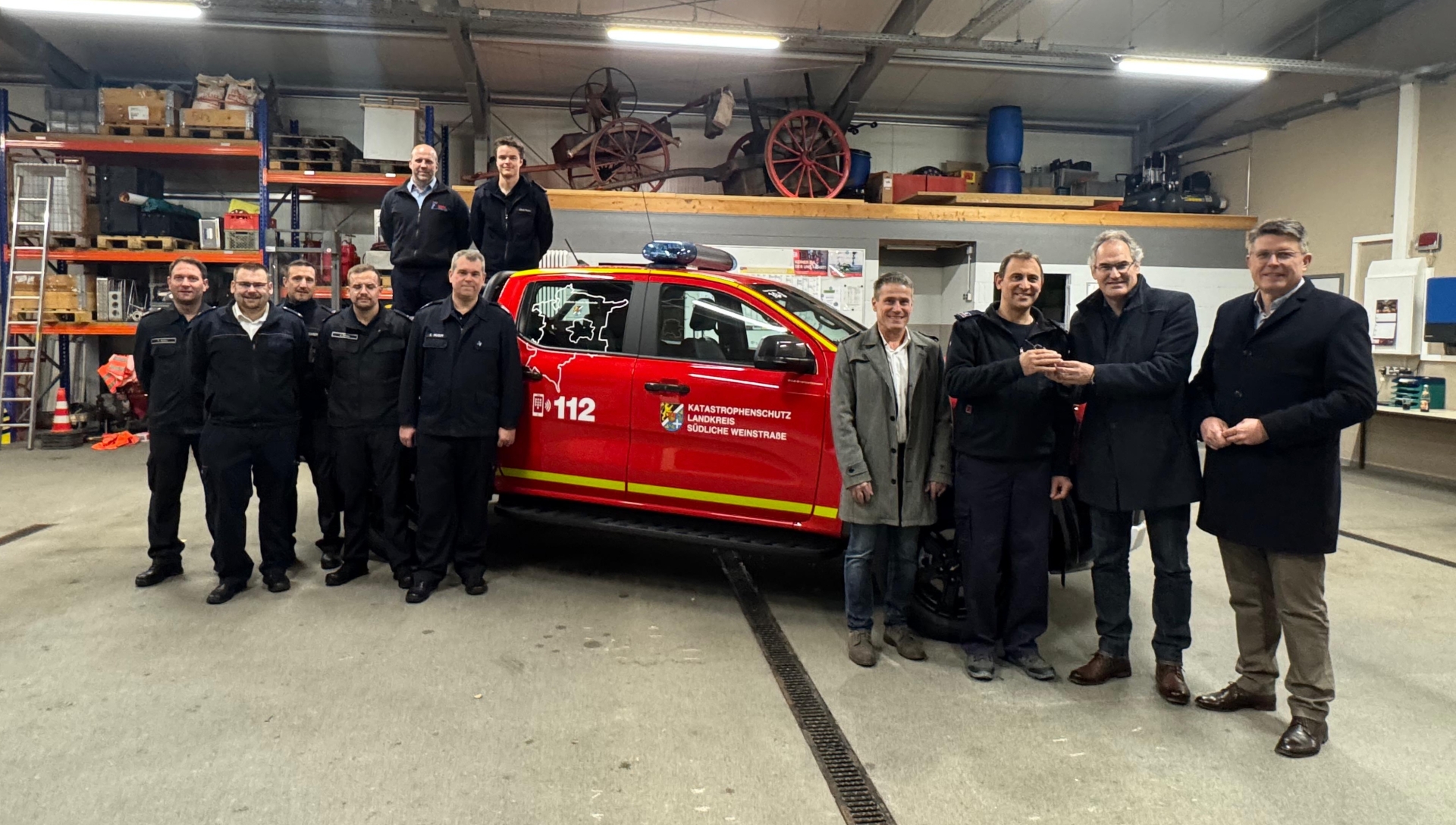 Mehrere Funktionsträger aus Kommunalpolitik und dem Brand- und Katastrophenschutz im Kreis SÜW stehen vor dem neuen KatSchutz-Fahrzeug beziehungsweise auf der Laderampe des Pickup.
