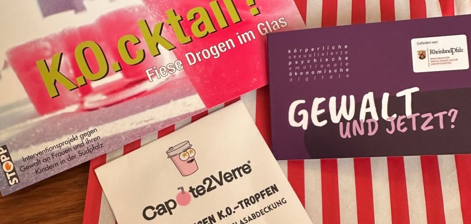 Verschiedene Informationsmaterialien zum Thema K.O.-Tropfen liegen auf einer rot-weiß-gestreiften Papiertüte.