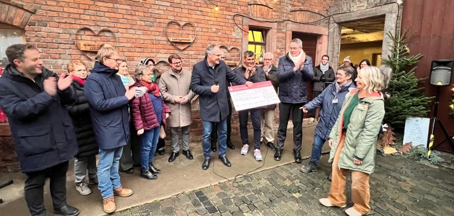Landrat Dietmar Seefeldt übergibt einen Spendenscheck, neben ihm stehen mehrere Menschen vor weihnachtlich geschmückter Wand.