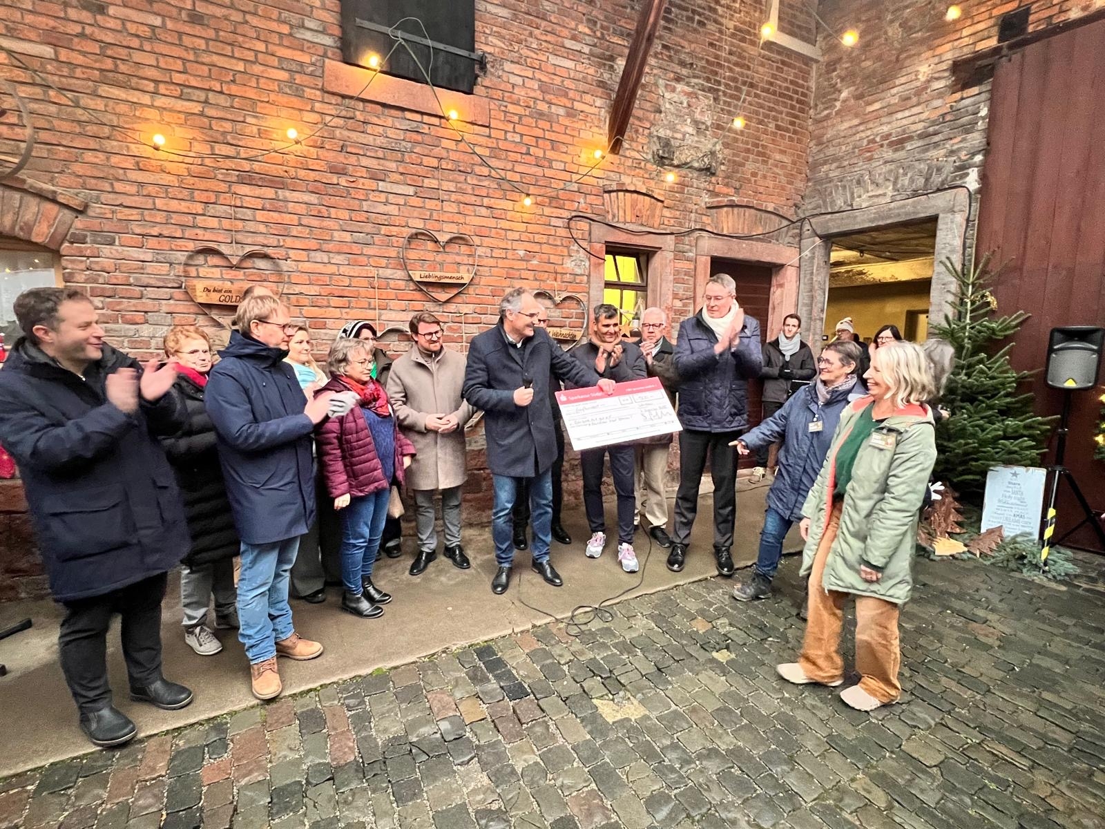 Landrat Dietmar Seefeldt übergibt einen Spendenscheck, neben ihm stehen mehrere Menschen vor weihnachtlich geschmückter Wand.