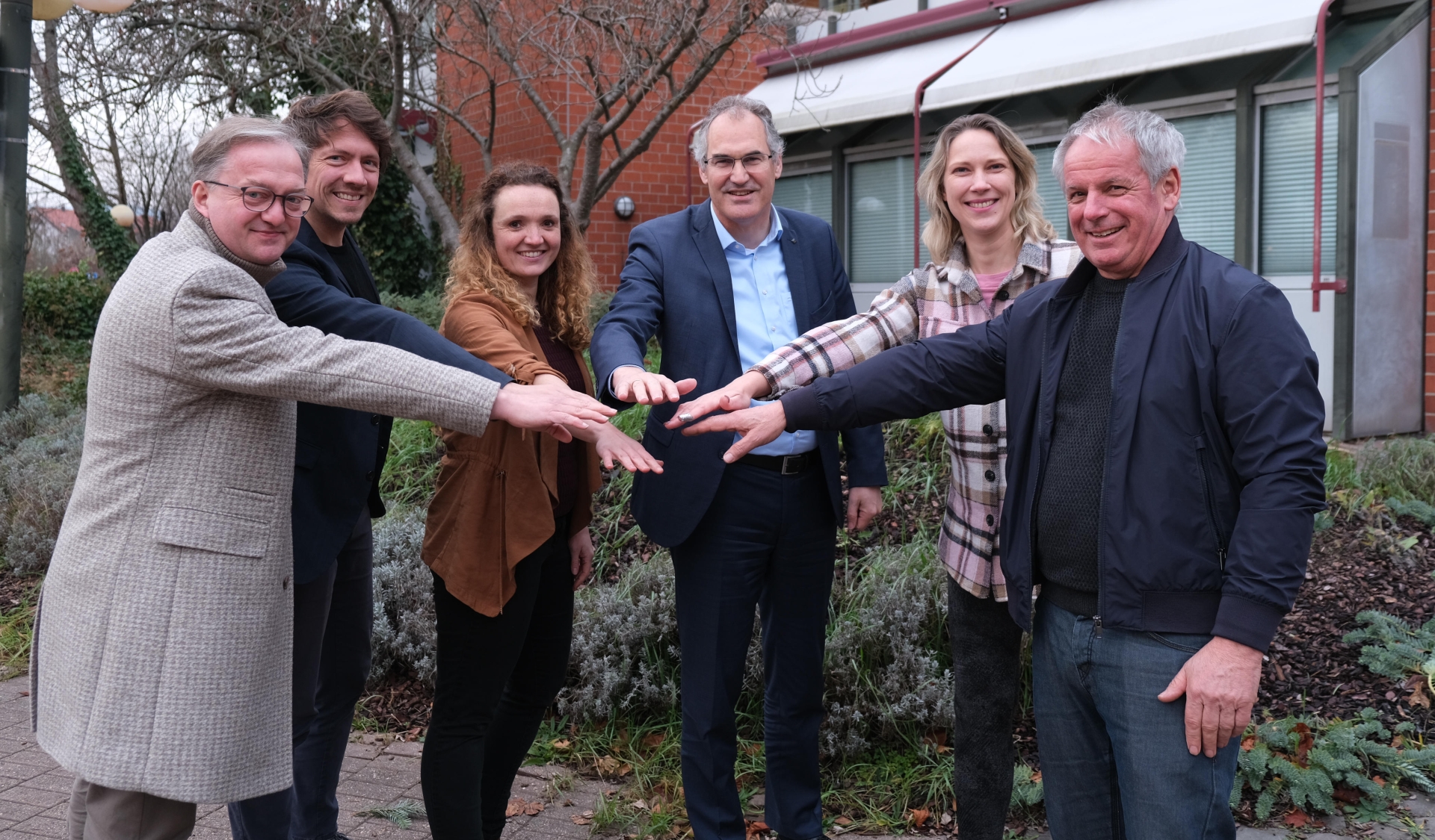 Sechs Personen stehen vorm Kreishaus und strecken jeweils eine Hand nach vorne.