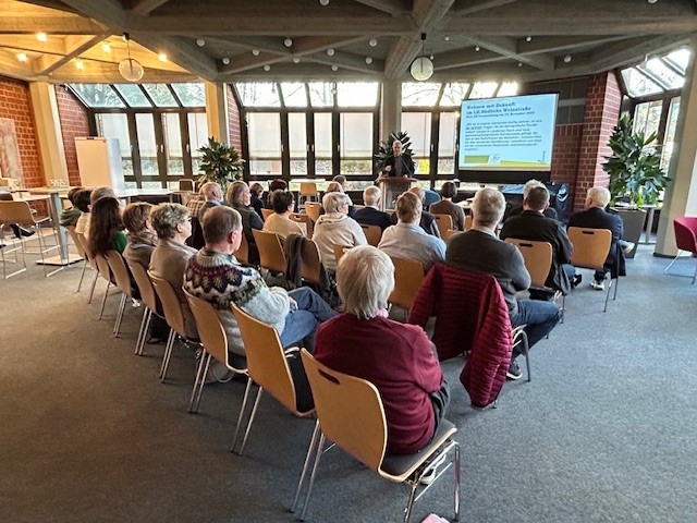 Menschen sitzen im Erdgeschoss der Kreisverwaltung und blicken auf eine Präsentationsfolie.
