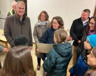 Landrat Dietmar Seefeldt steht inmitten einer Gruppe aus Erwachsenen und Kindern, die sich über die Übergabe eines symbolischen Schecks zur Unterstützung des Baus eines Jugendraums in Roschbach freuen.