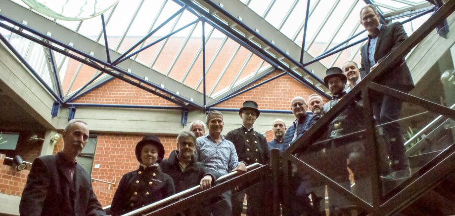 Thomas Cuntz, Isabell Göbel, Thomas Eichberger, Kreisbeigeordneter Werner Schreiner (hinten), Kreisbeigeordneter Uwe Huth (vorn), Andreas Jäger, Christian Wolf (Kreisverwaltung), Joachim Habermehl, Abteilungsleiter Peter Schürmann (Kreisverwaltung), Sven Leidner, Erster Kreisbeigeordneter Georg Kern und Landrat Dietmar Seefeldt (von links nach rechts) im Kreishaus. Foto: KV SÜW Gruppenbild der ausgeschiedenen und neuen Schornsteinfeger – drei von ihnen in traditioneller, schwarzer Kluft mit Hut – sowie der Mitglieder des Kreisvorstands SÜW auf der Treppe im Foyer des Kreishauses.