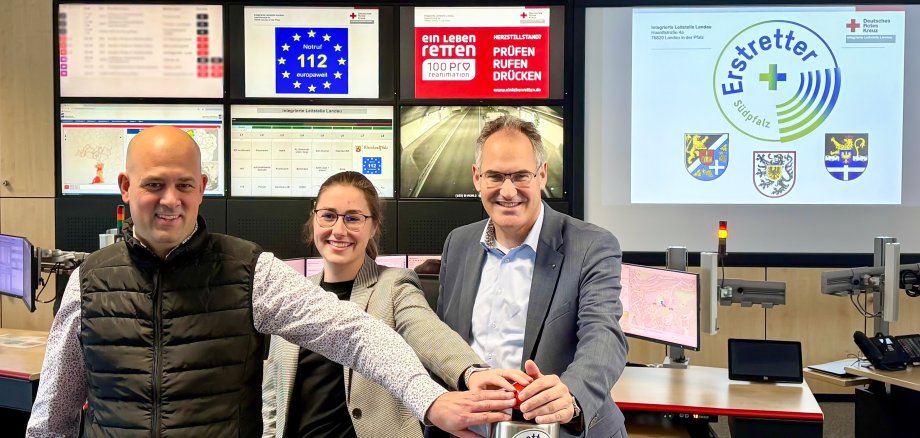 Drei Personen haben die Hand auf einem Auslöseknopf.