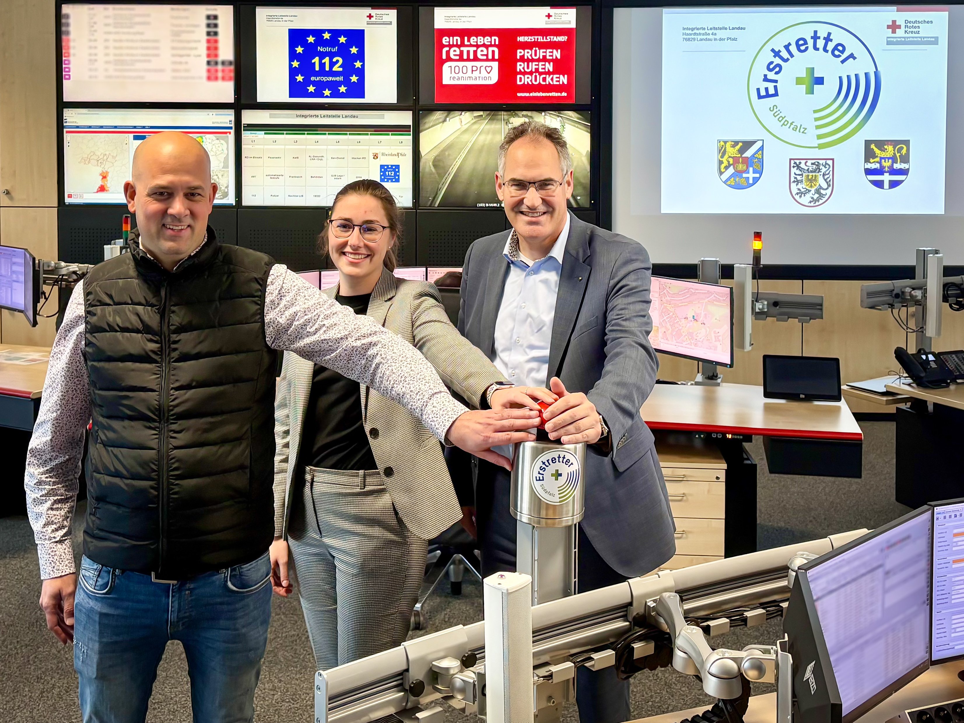 Drei Personen haben die Hand auf einem Auslöseknopf.