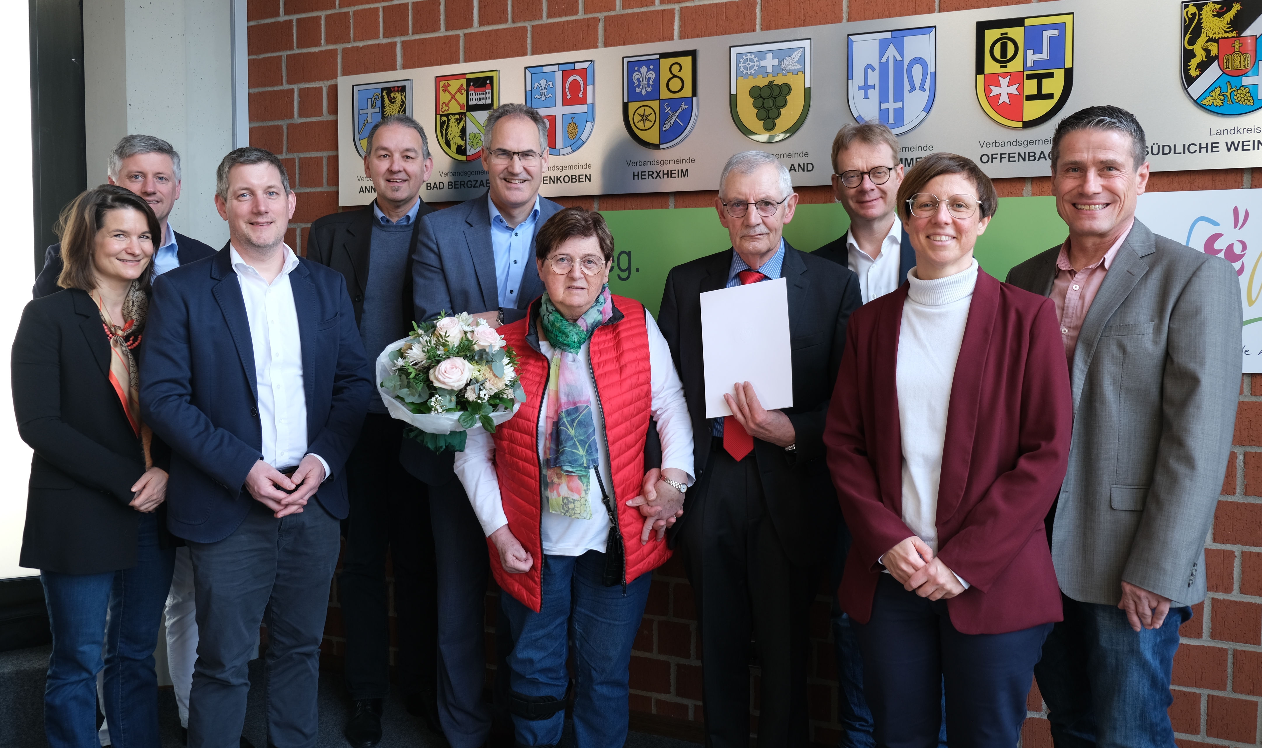 Eine Gruppe Menschen vor einer Backsteinwand mit Wappen.