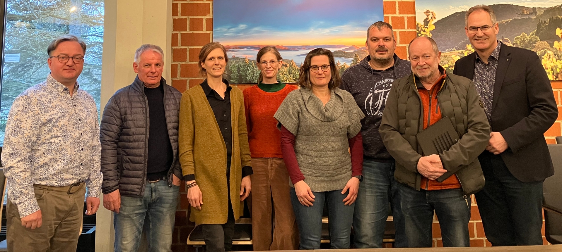 Gruppenbild: Ronny Bodenseh, kommissarischer Leiter der Schulabteilung der Kreisverwaltung SÜW, Kreisbeigeordneter Werner Schreiner, Monika Doppler-Meyer, Lena Bauer, Julia Weiter, Torsten Hertel und Silvester Hellmeister vom Schulelternbeirat des ETGA sowie Landrat Dietmar Seefeldt. Alle stehen nebeneinander vor einer Backsteinwand, an der zwei Landschaftsbilder hängen.