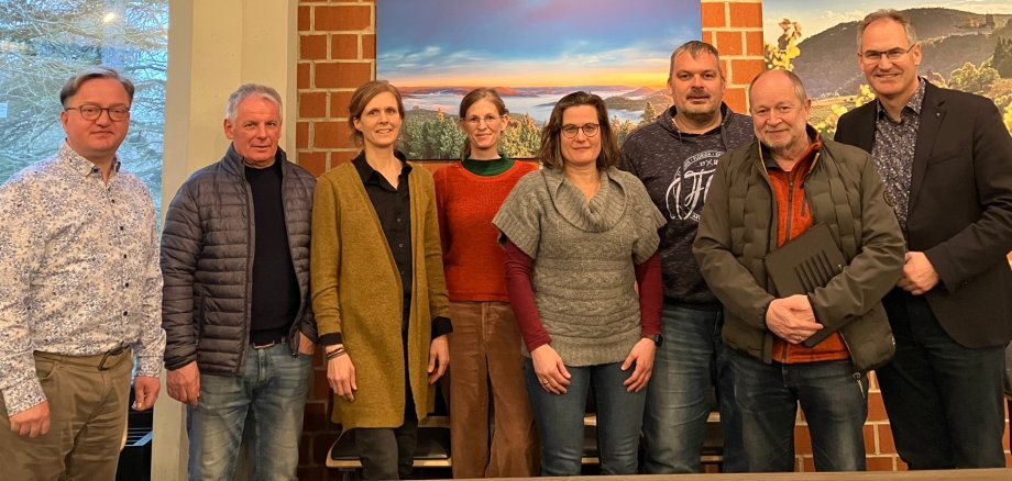 Tauschten sich im Kreishaus aus: Ronny Bodenseh, kommissarischer Leiter der Schulabteilung der Kreisverwaltung SÜW, Kreisbeigeordneter Werner Schreiner, Monika Doppler-Meyer, Lena Bauer, Julia Weiter, Torsten Hertel und Silvester Hellmeister vom Schulelternbeirat des ETGA sowie Landrat Dietmar Seefeldt (von links nach rechts). Foto: KV SÜW Gruppenbild: Ronny Bodenseh, kommissarischer Leiter der Schulabteilung der Kreisverwaltung SÜW, Kreisbeigeordneter Werner Schreiner, Monika Doppler-Meyer, Lena Bauer, Julia Weiter, Torsten Hertel und Silvester Hellmeister vom Schulelternbeirat des ETGA sowie Landrat Dietmar Seefeldt. Alle stehen nebeneinander vor einer Backsteinwand, an der zwei Landschaftsbilder hängen.