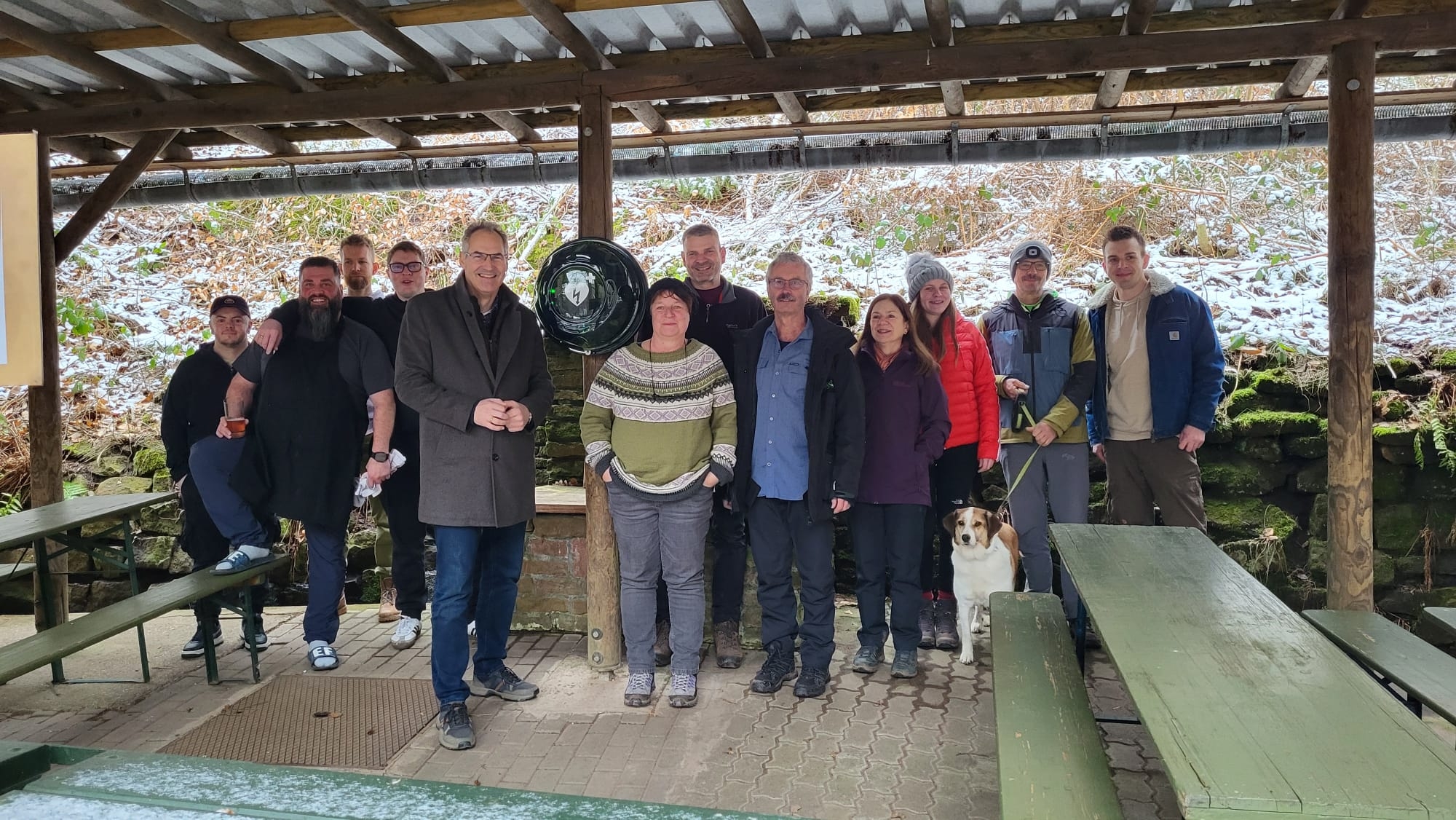 Unter einem Wellblech-Dach steht eine Gruppe Menschen.