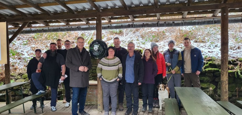 Unter einem Wellblech-Dach steht eine Gruppe Menschen.