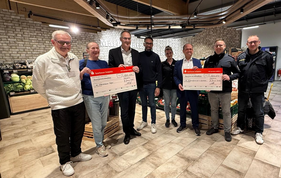 Acht Personen stehen in der Obst- und Gemüseabteilung des Edeka Kissel Marktes in Edesheim und halten zwei große symbolische Schecks in Händen.