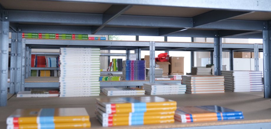 Blick durch ein Regalfach, in dem Schulbücher für die Schulbuchausleihe lagern. Im Hintergrund sind weitere Regale mit Schulbüchern zu sehen.