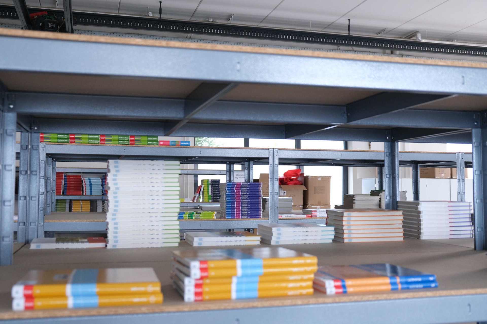 Blick durch ein Regalfach, in dem Schulbücher für die Schulbuchausleihe lagern. Im Hintergrund sind weitere Regale mit Schulbüchern zu sehen.