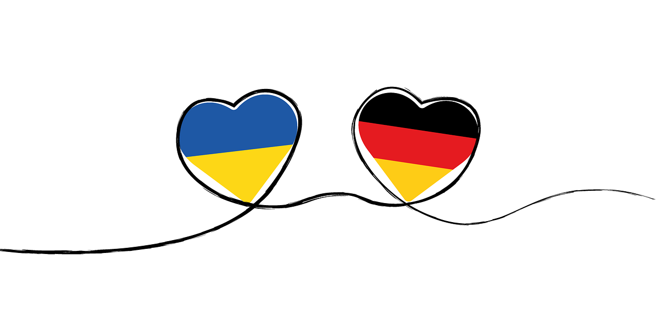 Zeichnung zweier Herzen, die durch eine schwarze Linie miteinander verbunden sind. Im Linken Herz sind die Farben der ukrainischen Flagge zu sehen, im rechten die der deutschen Flagge.