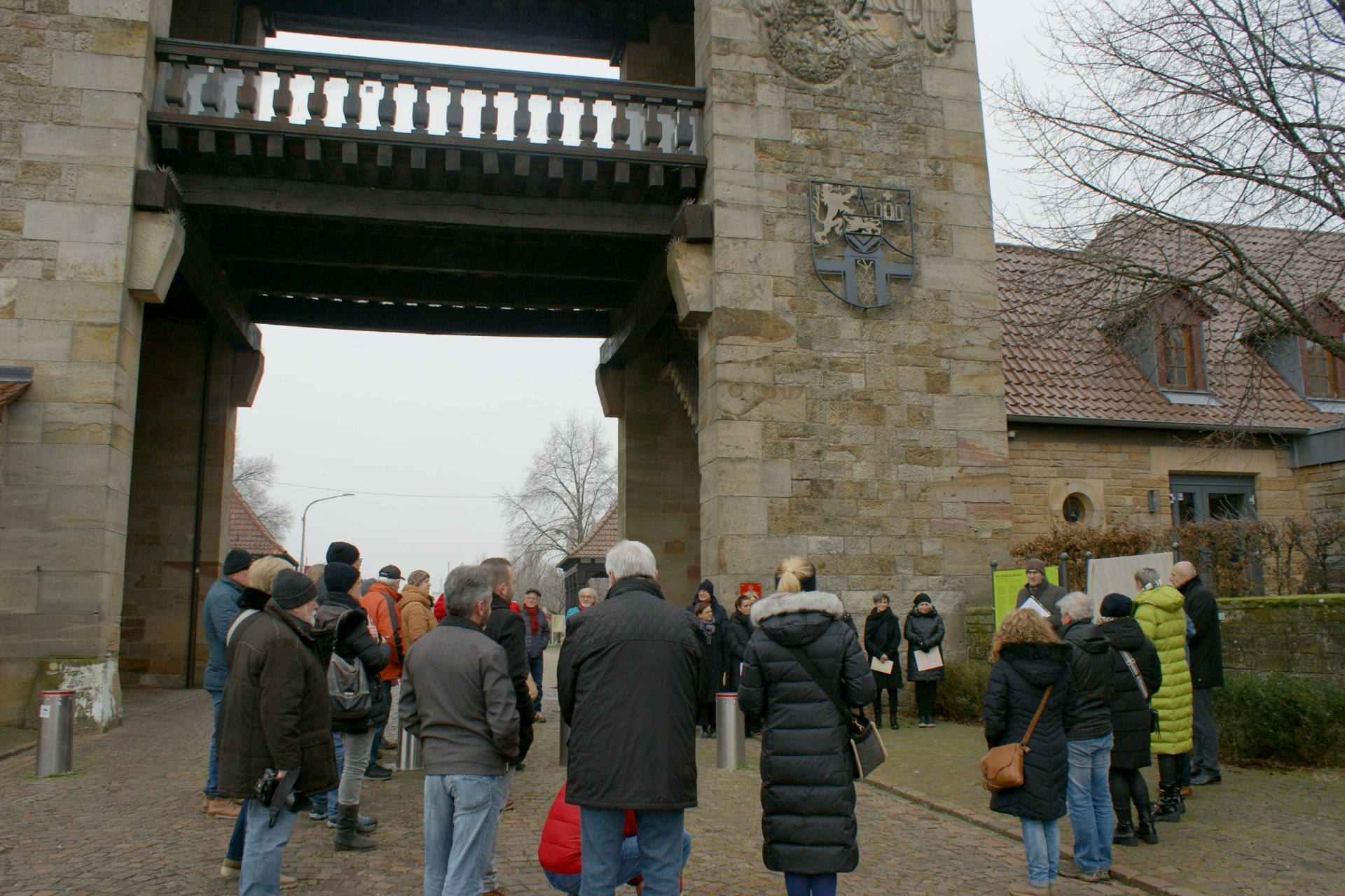 Blick auf die Feierstunde am Weintor, das mit dem Wappen des früheren Landkreises Bad Bergzabern und einem Sandsteinadler, der früher ein Hakenkreuz trug, verziert ist.