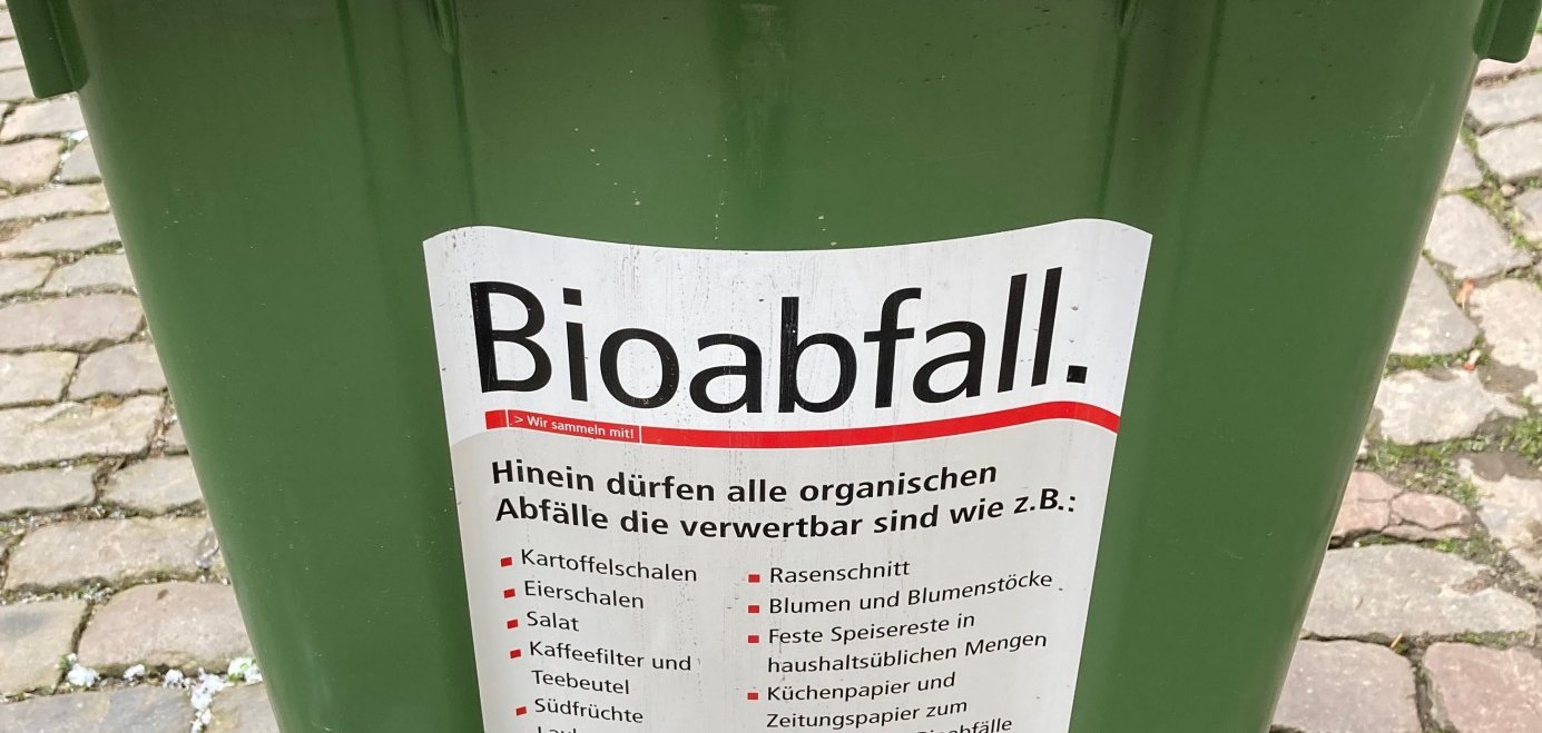 Nahaufnahme einer grünen Biomülltonne. Ein Aufkleber listet die Abfallarten auf, die in der Tonne entsorgt werden dürfen.