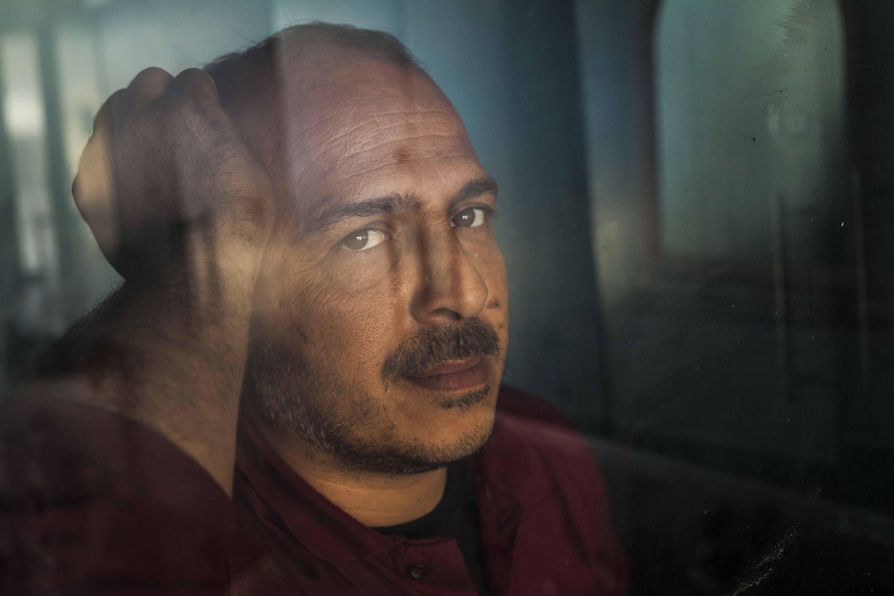 Nahaufnahme eines Mannes, der mit deprimierter Miene aus einem Fenster blickt.