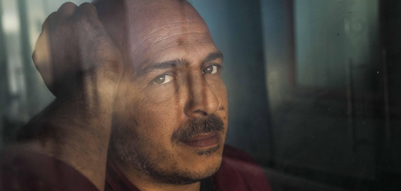 Nahaufnahme eines Mannes, der mit deprimierter Miene aus einem Fenster blickt.