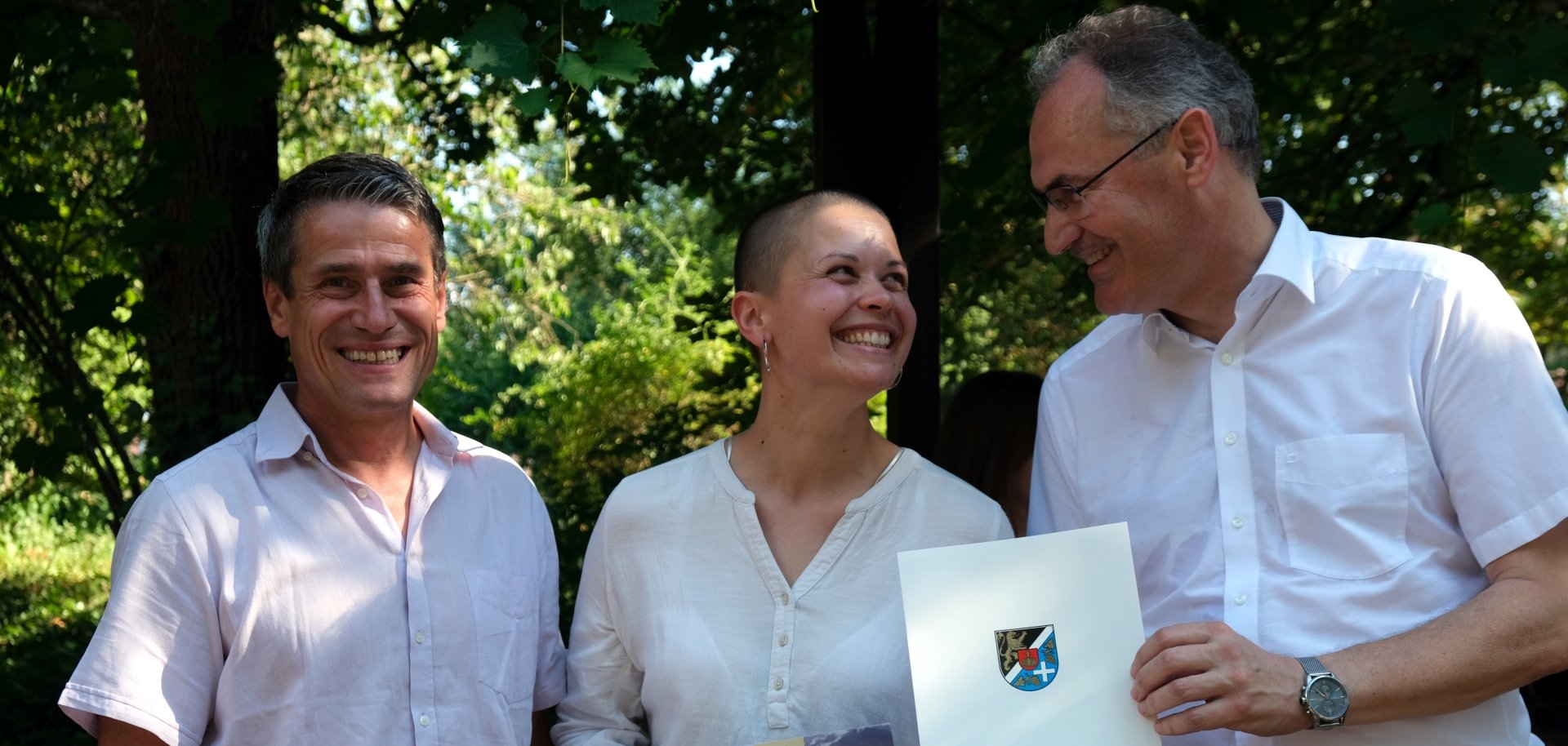 Landrat Dietmar Seefeldt (rechts) und Beigeordneter Uwe Huth gratulieren einer neu Eingebürgerten vor dem Kreishaus. Foto: KV SÜW