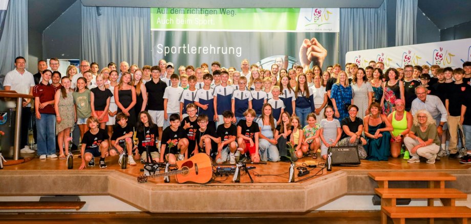 Die geehrten Sportlerinnen und Sportler, der Landrat sowie weitere Vertretungen der Politik und der Kreisverwaltung stehen gemeinsam in mehreren Reihen auf einer Bühne und lächeln in die Kamera.