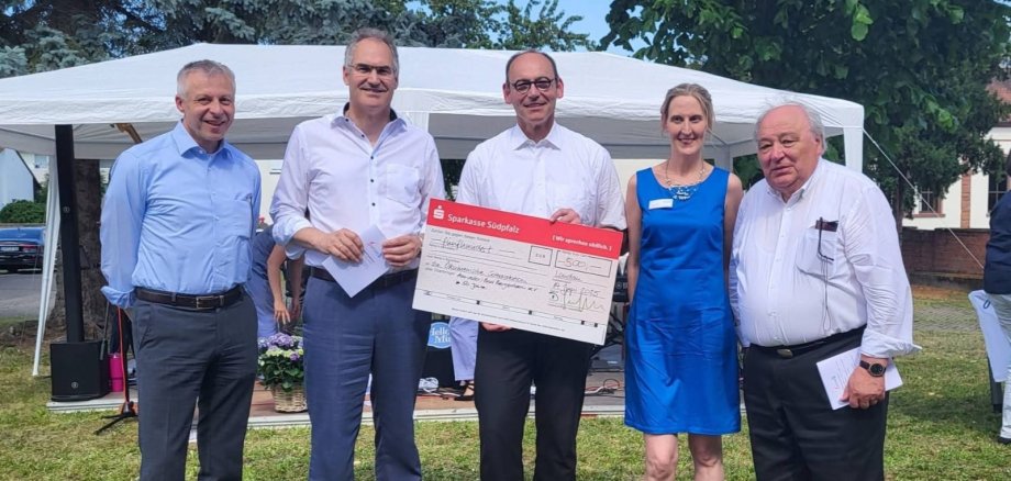Landrat Dietmar Seefeldt und die Verantwortlichen der Ökumenischen Sozialstation stehen in einer Reihe vor einem weißen Pavillon. Der Mann in der Mitte hält einen Spendenscheck in der Hand.