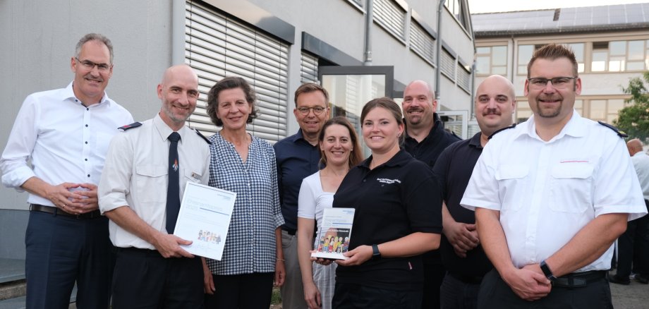 Mehrere Personen im Halbkreis, zwei Menschen halten je eine Urkunde und eine Stele, den Preis, in der Hand.
